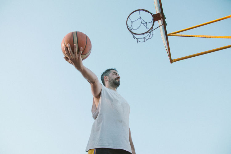 Man playing basketball while standing against sky