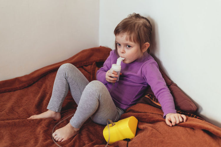 Sick child lies in bed and makes inhalation using a nebulizer.