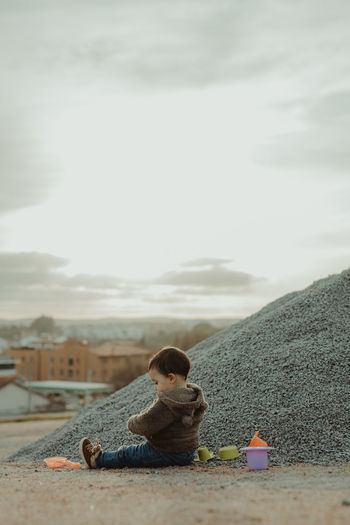 Child sitting on land against sky