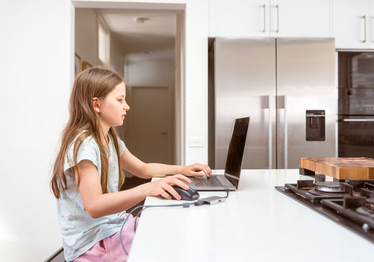 Close up of young girl using mouse with laptop in kitchen 