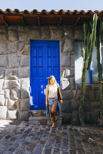 A young woman is standing near a blue old door in cusco, peru