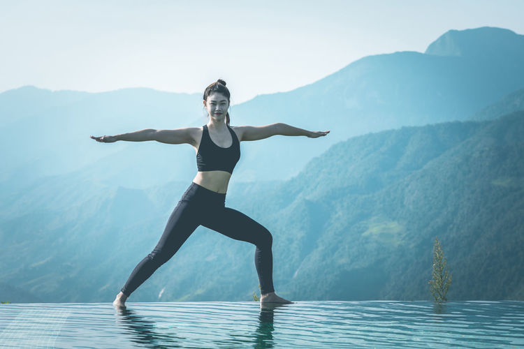 Full length portrait of woman exercising at infinity pool against mountains