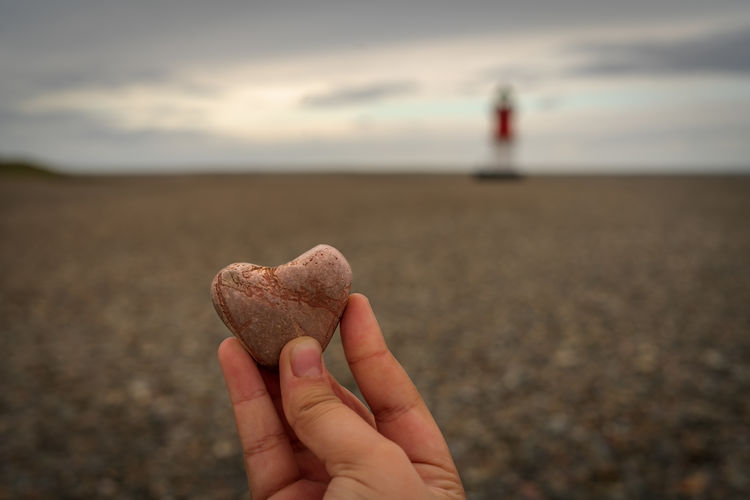 Man holding heart shape stone at beach against sky