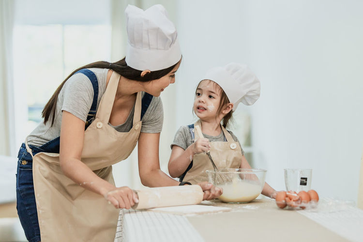 Mother and daughter standing on cutting board in kitchen