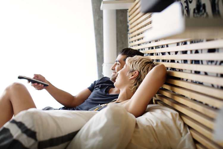 Happy couple watching tv while lying on bed at home