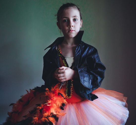 Portrait of confident girl wearing tutu and jacket against wall