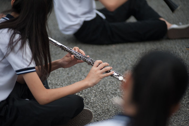 School girls playing flutes while sitting on footpath