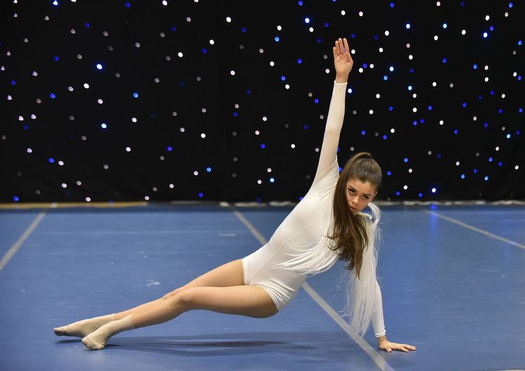 Young teenage girl in white jersey perform modern dance on stage