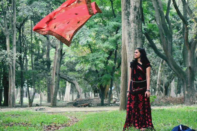 Woman looking at red dupatta in mid-air at park