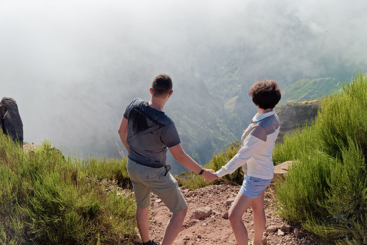 High angle view of couple holding hands standing on mountain during foggy weather