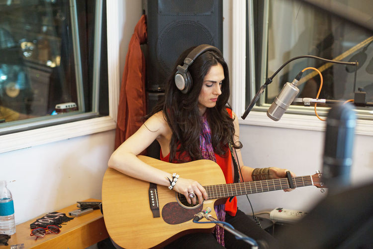 Young woman playing acoustic guitar at a recording studio
