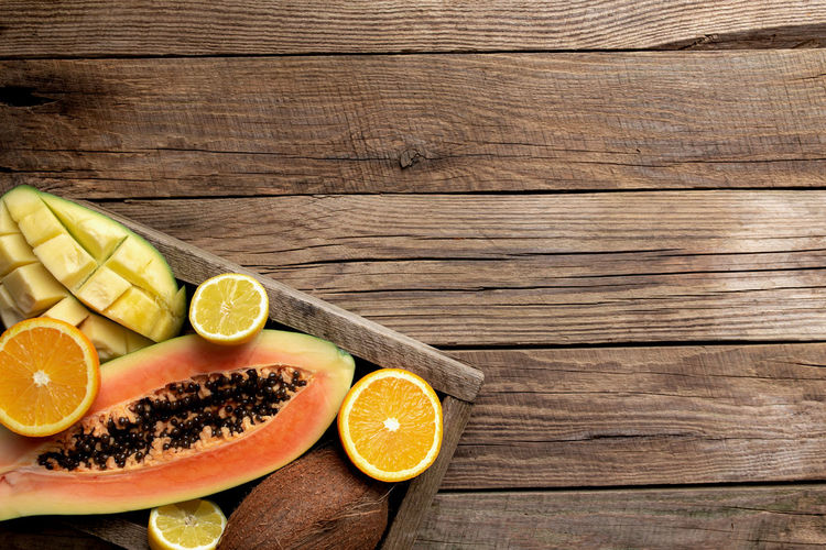Fresh tropical fruits in a wooden delivery box on a wooden background. papaya, orange, coconut
