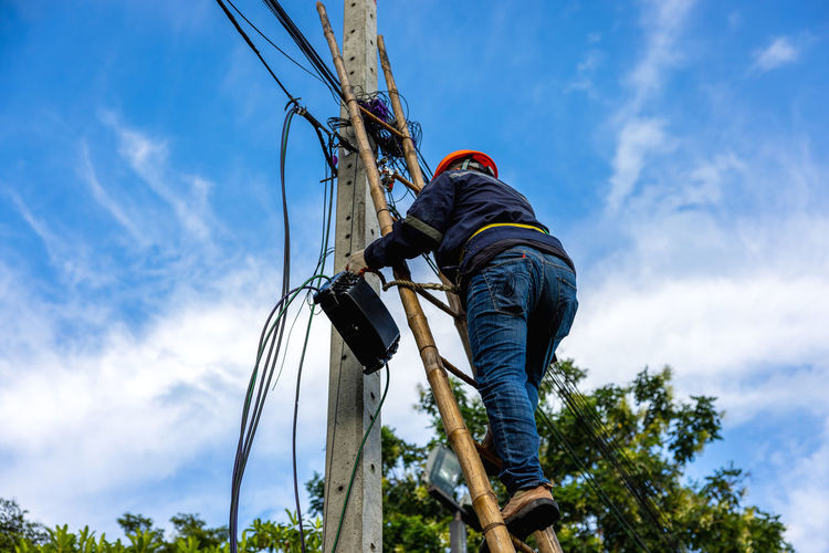 Low angle view of man standing on rope against sky