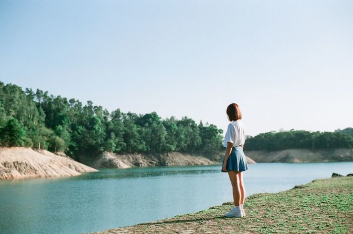 Young woman standing by river against clear sky