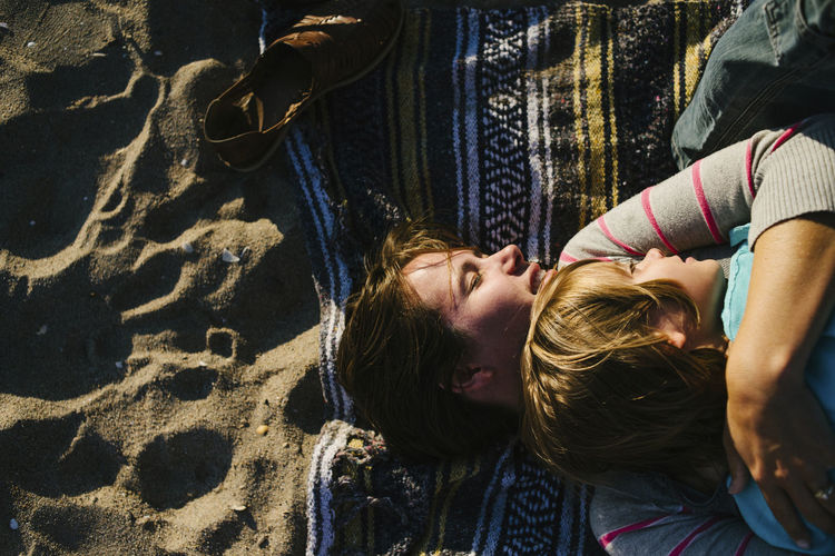 Overhead view of woman embracing daughter while lying on beach towel