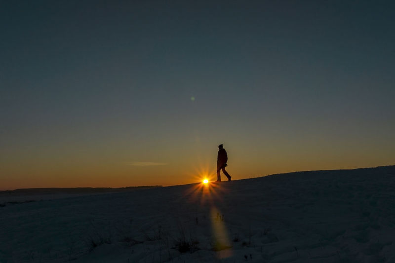 Silhouette of man at sunset walking in winter, setting sun, landscape, scenic nature. travel alone 