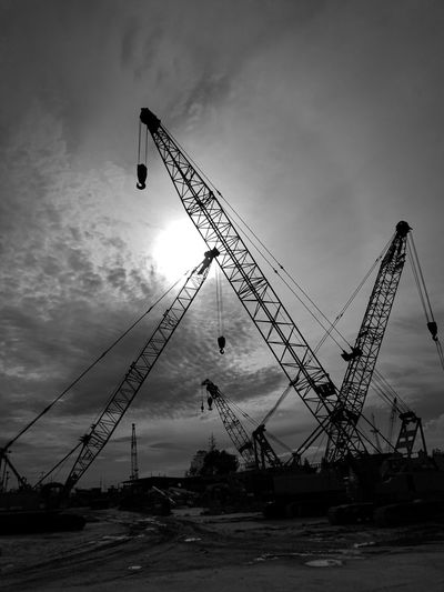 Low angle view of cranes at construction site against sky