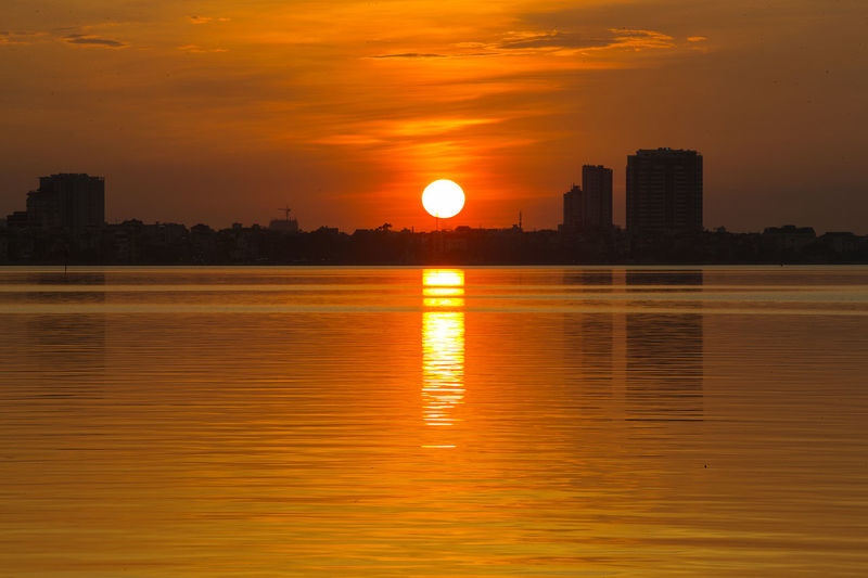 Scenic view of sea and buildings against orange sky