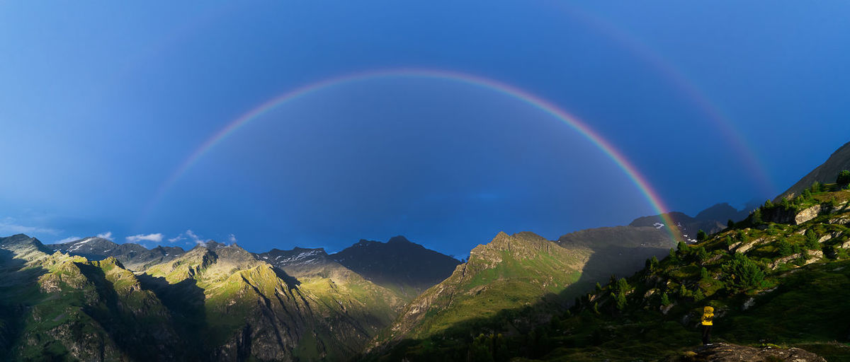 Scenic view of rainbow over mountains against blue sky
