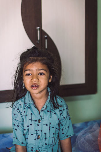 Portrait of cute girl sitting on bed at home