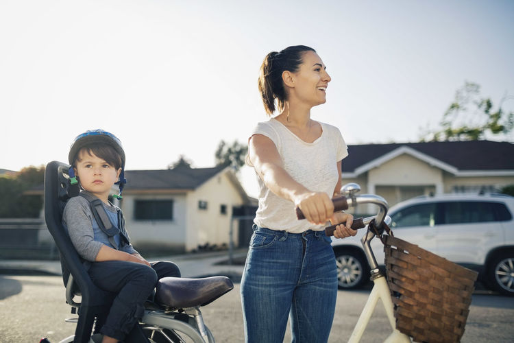 Happy woman looking away while son sitting on bicycle outdoors