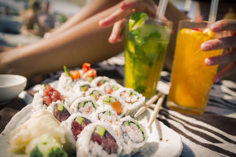 Close-up of sushi with woman holding cocktail glasses
