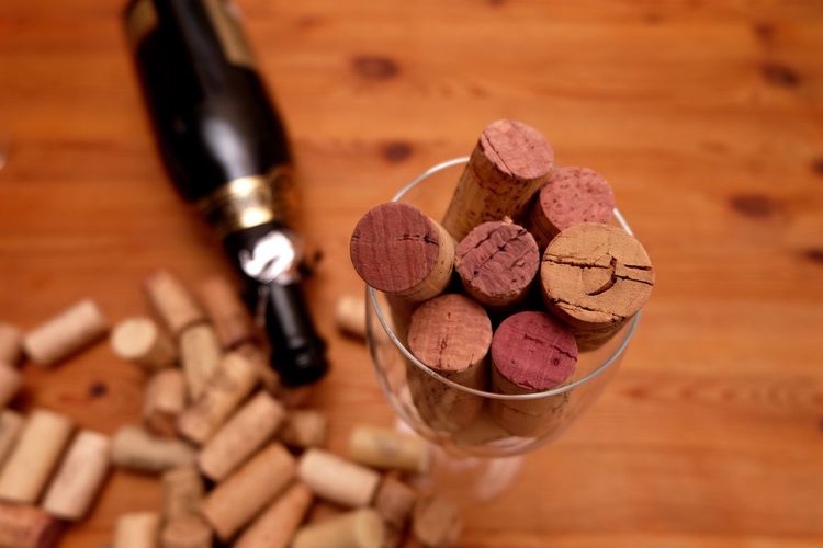 High angle view of corks in wineglass by wine bottle on wooden table