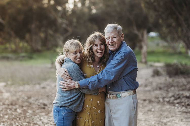Portrait of adult woman and senior parents hugging at park