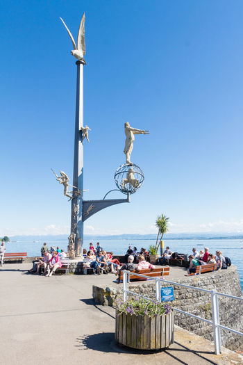 People at promenade by lake constance against clear blue sky
