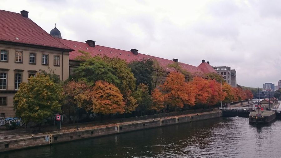 Canal in front of buildings in town against cloudy sky