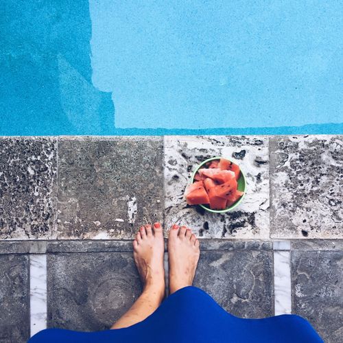 Low section of woman standing by watermelon in bowl at poolside