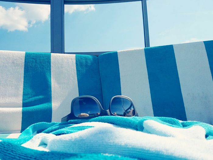 Sunglass and towel on deck chairs against glass window