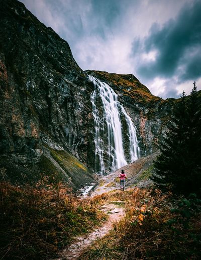 Rear view of woman looking at waterfall falling from mountain against sky