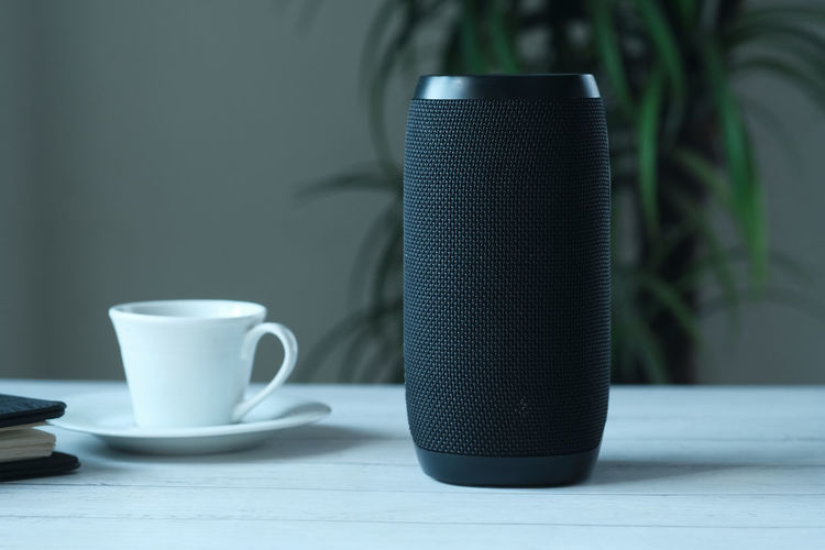 Smart speaker and tea cup on wooden table.