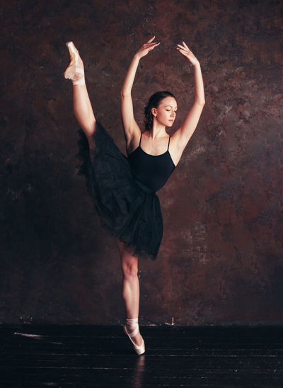 Full length of young woman with arms raised dancing against wall in dance studio