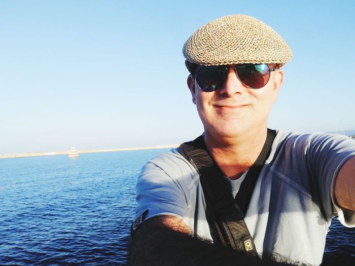 Portrait of man wearing sunglasses and cap against sea