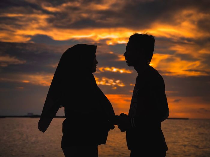 Side view of couple standing by sea during sunset