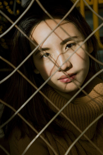 Close-up portrait of woman seen through fence