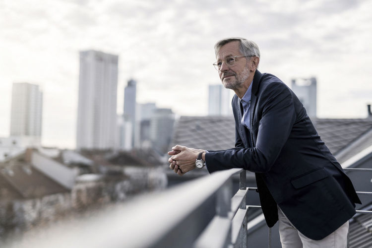 Grey-haired businessman standing on balcony looking over city