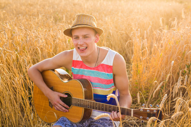 Smiling young man playing guitar on field