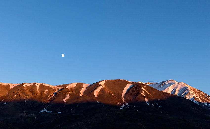 Sunset in the andes mountain range with the moon on the horizon