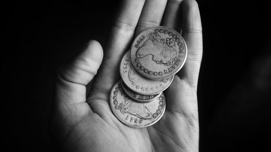 Cropped hand of person holding coins against black background