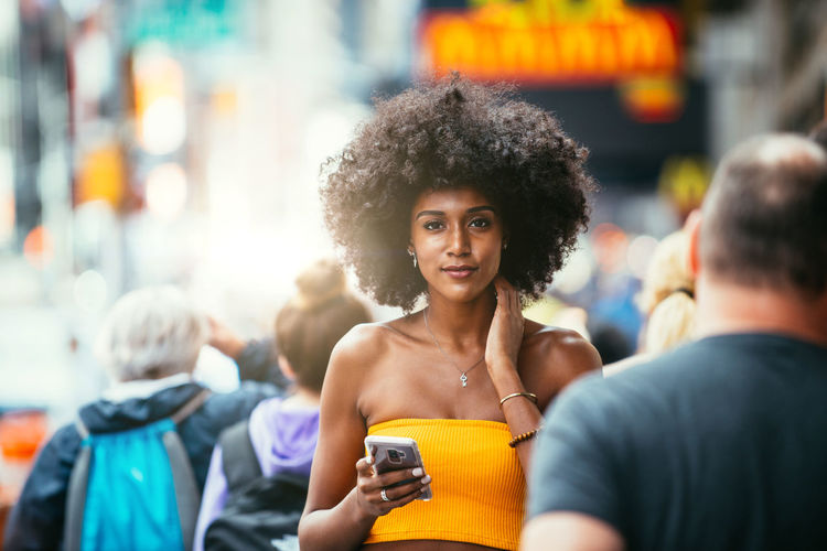 Portrait of confident young woman holding smart phone on city street