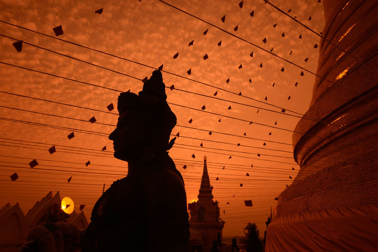 Low angle view of decorations and stature at temple against orange sky during sunset