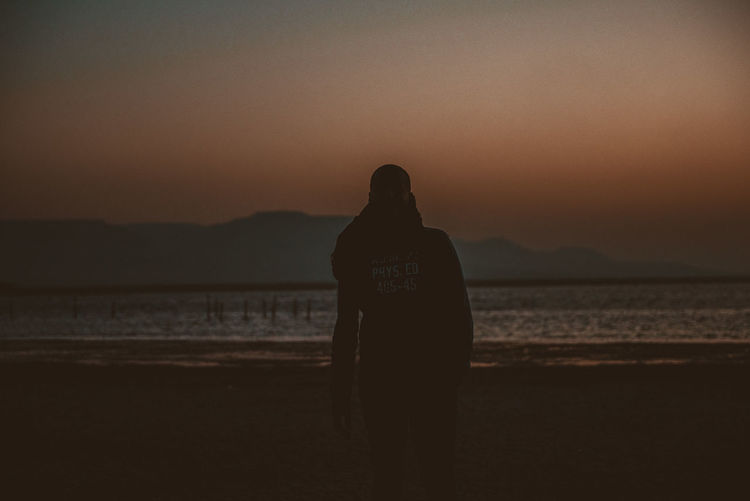 Silhouette man standing at beach against sky during sunset