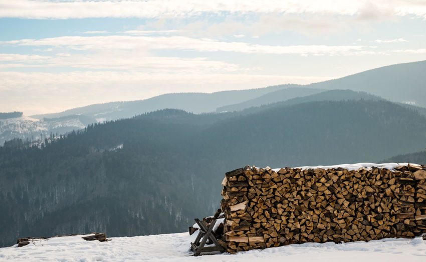 Stack of logs on snow covered mountains against sky