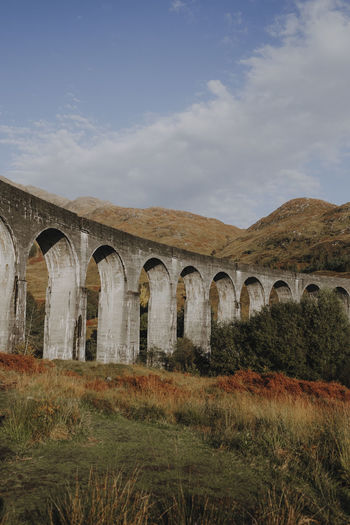Low angle of old railway viaduct in scottish highland against mountains and blue cloudy sky in autumn day