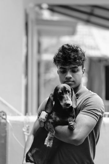 Young man carries dachshund puppy in his arms
