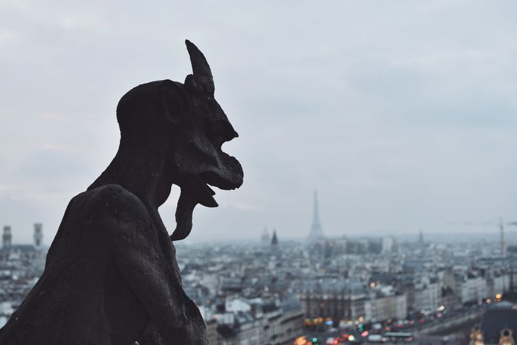 Gargoyle against cityscape during sunset