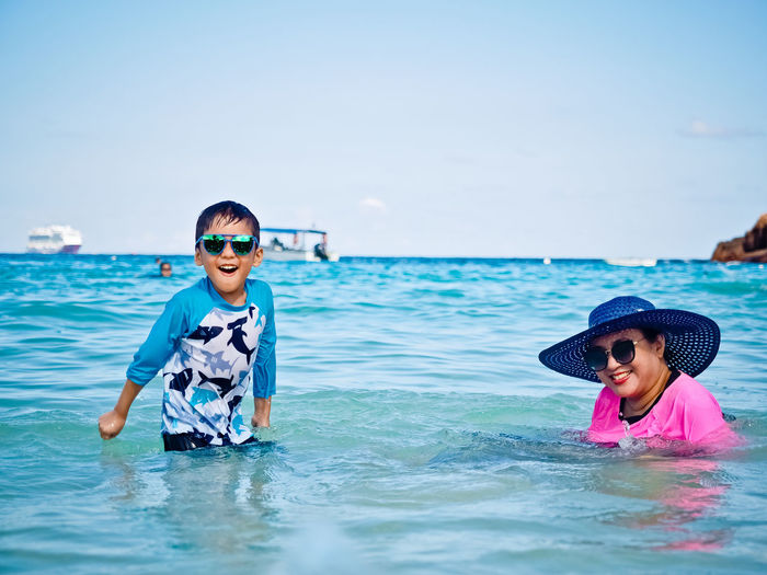 Portrait of smiling boy and woman in sea against sky